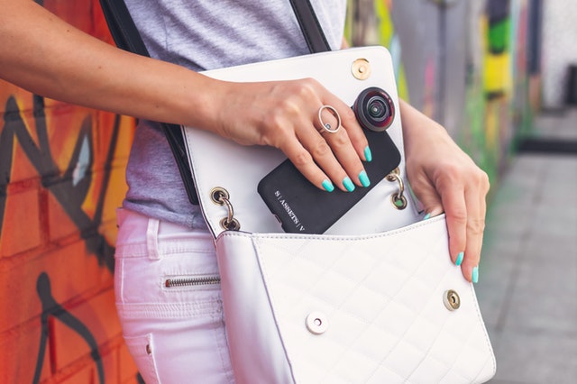 Detail ženské ruky vkládající telefon do bílé kabelky
